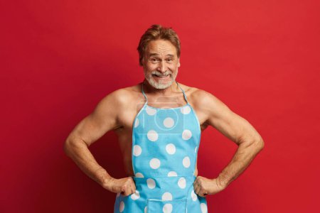 Photo for Smiling Man Posing Studio. Bearded Grandfather In Apron On Naked Torso Feeling Content Emotions And Posing Isolated On Red Background Studio - Royalty Free Image