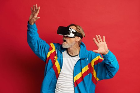 Téléchargez les photos : Homme âgé essayant VR. Portrait de grand-père étonnant Découvrir les nouvelles technologies Porter un casque de réalité virtuelle, Vision 3D futuriste. Studio intérieur isolé sur fond rouge - en image libre de droit
