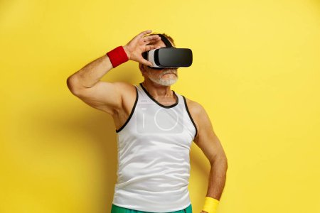 Téléchargez les photos : Focused Man Essayant VR. Portrait de l'homme âgé Découvrir les nouvelles technologies Porter un casque de réalité virtuelle, Vision 3D futuriste. Studio intérieur isolé sur fond jaune - en image libre de droit