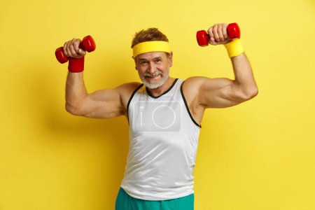 Photo for Senior Man Training With Dumbbells. Glad Grandfather Raising Arms With Dumbbells, Satisfied After Having Training In Gym Isolated Over Yellow Wall Empty Space - Royalty Free Image
