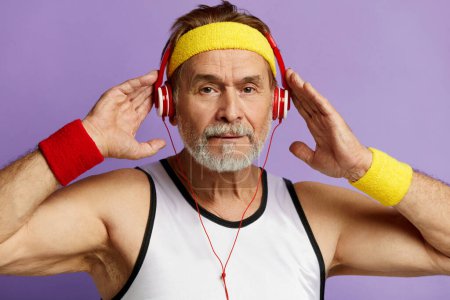 Foto de Música Escuchando. Positive Grandfather Listening Favourite Song on Radio Wearing Earphones and Dancing (en inglés). Estudio interior filmado aislado sobre fondo violeta - Imagen libre de derechos
