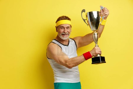 Photo for Sportsman award . Mature Man Smiling Happily, Holding Golden Prize, Glad To Win Isolated On Yellow Background - Royalty Free Image
