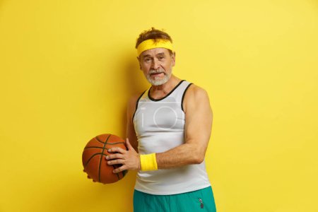 Photo for Sport Man Playing Basketball. Bearded Grandfather Holding Basketball Ball Standing Over Isolated Yellow Background. Sport Concept - Royalty Free Image