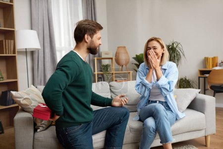 Photo for Happy Man Presenting Gift To Wife. Excited Young Man Presenting Good Unexpected Present To Wife At Home. Loving Boyfriend Making Romantic Surprise To Girlfriend - Royalty Free Image