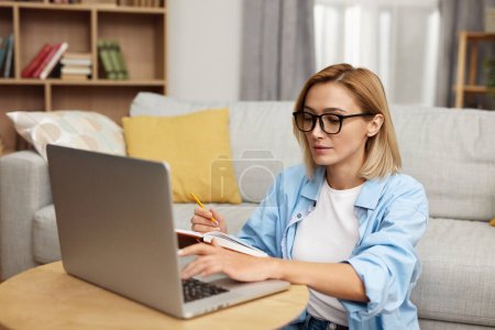 Téléchargez les photos : Smiling Woman Working Laptop. Nice Beautiful Lady With Blonde Hair Work At Notebook At Home. Technology Woman Concept - en image libre de droit