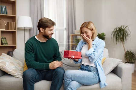Happy Man Presenting Gift To Wife. Excited Young Man Presenting Good Unexpected Present To Wife At Home. Loving Boyfriend Making Romantic Surprise To Girlfriend 
