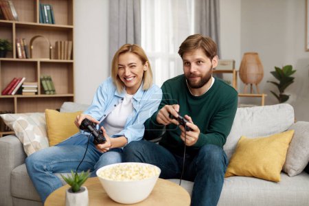 Photo for Happy Couple Playing Video Games. Boyfriend And Girlfriend Sitting On Couch In Living Room Enjoying Playing Video Games And Spending Time Together. Enjoying Moment On Weekend Concept - Royalty Free Image