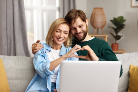 Foto de Couple Using Laptop Computer, While Sitting On The Living Room of Their Apartment. Boyfriend and Girlfriend Talk, Shop on Internet, Choose Product to Order Online, Watch Streaming Service - Imagen libre de derechos