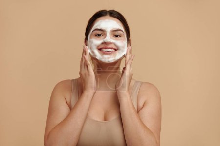 Téléchargez les photos : Cleaning Face. Smiling Full Figured Woman Cleaning Facial Skin with Foam Soap. Happy Girl Cleansing Face Applying Facial Cleanser Closeup. High Resolution - en image libre de droit