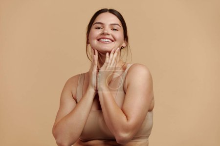 Téléchargez les photos : Smiling Woman Touching Face. Waist up Portrait of Attractive Woman Touching her Skin and Smiling While Applying Moisturiser. Woman Appearance and Skin Care Concept - en image libre de droit
