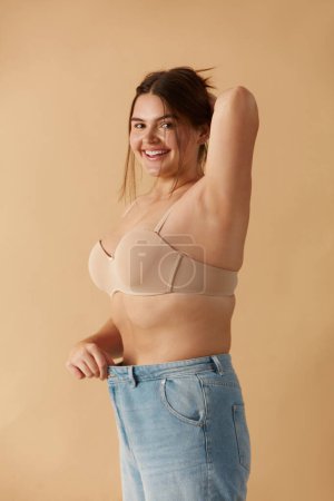 Foto de Plus Size Woman in Jeans. Overweight Smiling Woman Demonstrating Weight Loss. Happy Girl Showing Large Jeans And Looking At Camera - Imagen libre de derechos