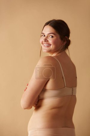 Photo for Full Figured Woman. Happy Curvy Oversize Woman Posing In Beige Lingerie At Studio. Confident Plus Size Lady Smiling Indoors. Body Imperfection, Body Acceptance, Body Positive And Diversity Concept - Royalty Free Image