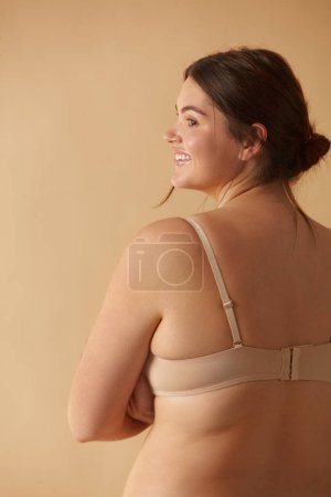 Photo for Plus Size Woman. Back View Of Happy Full Figured Woman Posing In Beige Lingerie At Studio. Confident Plus Size Lady Smiling Indoors. Love Yourself Concept - Royalty Free Image