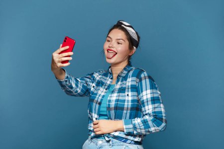 Foto de Happy Woman Making Selfie Smartphone. Plus Size Girl Showing Tongue While Videocalling Cellphone, Shooting Content For Social Media, Enjoying Mobile - Imagen libre de derechos