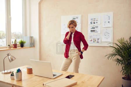 Téléchargez les photos : Young Businesswoman Standing At Workplace. Serious Woman Thinking Office. Blonde Lady Watching Laptop Computer Indoors - en image libre de droit
