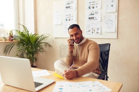 Smiling Businessman Calling Smartphone. Positive Multiracial Man Talking On Phone in Office Alone. Happy Guy Holding Mobile And Writing Notes. Business concept 