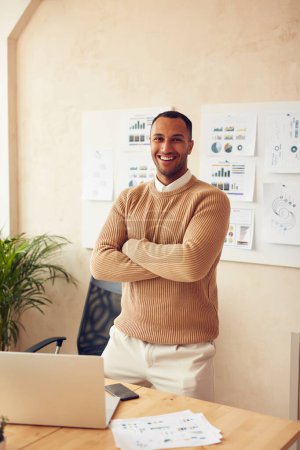 Foto de Smiling Businessman In Office. Multiracial Guy In Casual Clothes Posing Arms Crossed. Businessman Smiling And Looking At Camera - Imagen libre de derechos