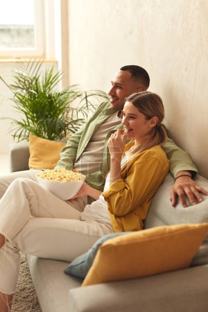 Téléchargez les photos : Happy Couple Watching TV At Home. Loving People Resting On Sofa And Eating Popcorn At Cozy Home Morning. Leisure Concept - en image libre de droit