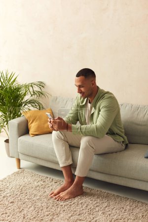 Téléchargez les photos : Man Using Smartphone At Home. Handsome Multiracial Guy Sitting On Sofa And Messaging In Cozy Living Room at Home. Male Person Doing Online Shopping, Browsing Internet and Checking Social Media - en image libre de droit