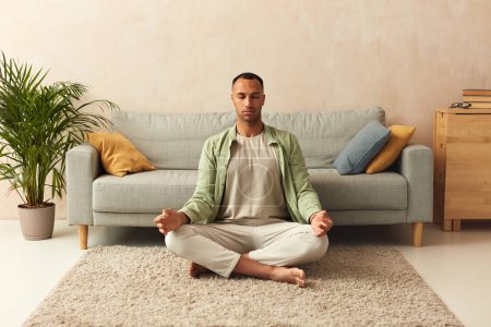 Téléchargez les photos : Calm Man Meditating Home. Multiracial Guy Sitting In Lotus Pose Practicing Yoga At Home. Sport, Fitness And Healthy Lifestyle Concept - en image libre de droit