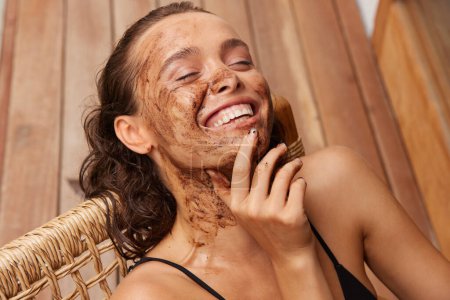 Foto de Face Care. Smiling Young Woman With Natural Makeup And Coffee Scrub Mask On Fresh Facial Skin. Portrait Of Beautiful Sexy Female Model With Peeling Cosmetic Product On Beauty Face - Imagen libre de derechos