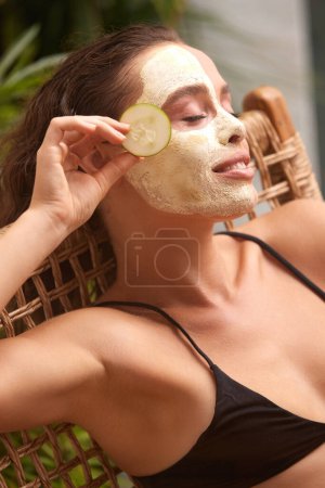 Foto de Face Mask Girl Hold Slice of Cucumber. Happy Young Relaxed Woman Enjoying Skin Care Routine at Street. Concept of Skincare - Imagen libre de derechos