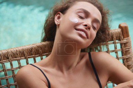 Photo for Skin Care Woman With Cream on Face. Sexy Woman In Bikini Sunbathing With Cosmetic Cream On Skin Under Eyes Near Swimming Pool In Summer. Young Female With Beauty Product On Soft Skin - Royalty Free Image
