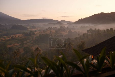 Foto de Una hermosa mañana en Bali con niebla rodando sobre las montañas mientras sale el sol, creando un impresionante paisaje natural. - Imagen libre de derechos