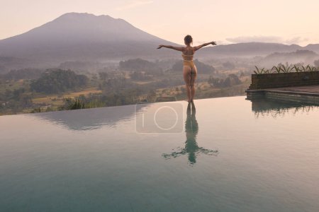 Téléchargez les photos : Belle femme bénéficiant d'une piscine dans les montagnes. Jeune femme au corps sexy en maillot de bain beige reposant sur la piscine en bois contre le paysage volcanique tropical à Bali, Indonésie - en image libre de droit