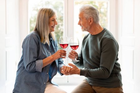 Téléchargez les photos : Couple adulte dégustant du vin et conversation au .home. Accueil Adultes souriants profitant d'une célébration. - en image libre de droit