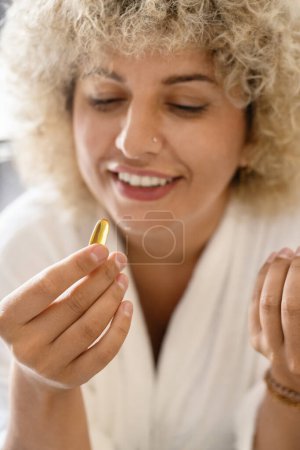 Foto de Dieta saludable. Mujer joven feliz sosteniendo Omega-3 cápsula, suplemento diario de salud. Joven hembra mira una cápsula dorada Omega-3 en su mano. Estilo de vida saludable y suplementos nutricionales. - Imagen libre de derechos