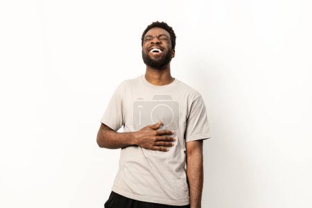 Photo for A cheerful African man laughing sincerely, hand on stomach, isolated on a white background with visible joy and contentment. - Royalty Free Image