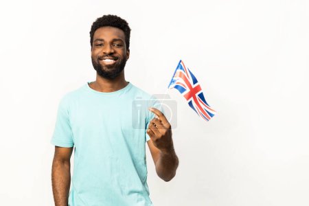 Photo for Joyful African American male showcasing patriotism by holding a small United Kingdom flag, isolated on a white background, expressing positive emotions and cultural pride. - Royalty Free Image