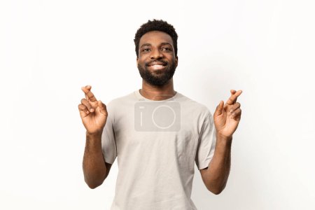 Photo for Portrait of a cheerful man crossing fingers for good fortune, smiling against a white background with positive vibes. - Royalty Free Image