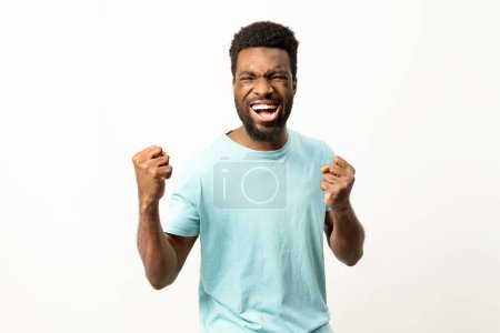 Foto de Hombre afroamericano enérgico animando con los puños cerrados en un gesto triunfante sobre un fondo liso. - Imagen libre de derechos
