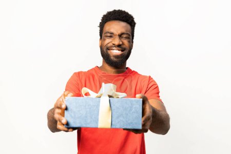 Cheerful African American man presenting a wrapped gift box with a joyous smile, isolated on a white background. Concept of celebration, generosity, and sharing.