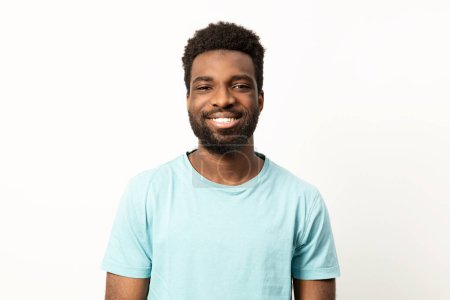 Foto de Retrato de un joven afroamericano feliz con una sonrisa brillante, posando sobre un fondo limpio y llano en una camiseta casual. - Imagen libre de derechos