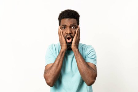 Surprised African American male in a blue t-shirt with a stunned expression against a clean, white backdrop.
