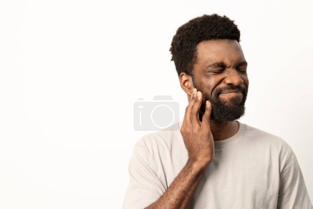 Téléchargez les photos : Homme adulte avec expression faciale affligée tenant sa joue en raison d'un mal de dents douloureux sur un fond blanc. - en image libre de droit