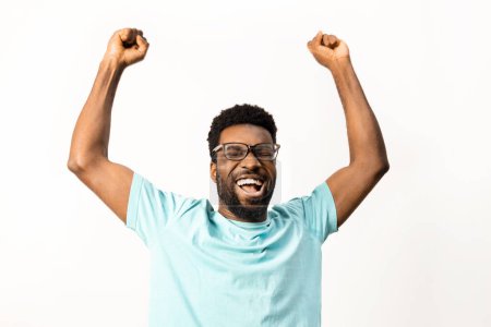 Foto de Hombre afroamericano con gafas celebrando una victoria, brazos levantados en emoción, aislados sobre un fondo blanco, transmitiendo felicidad y emociones positivas. - Imagen libre de derechos