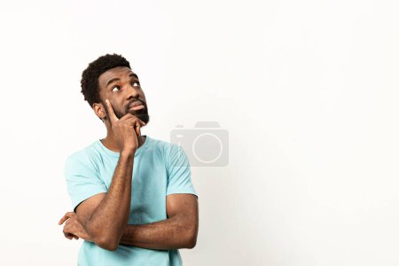 Photo for Pensive African American male in a blue shirt lost in thought, with a contemplative expression, isolated on white. - Royalty Free Image