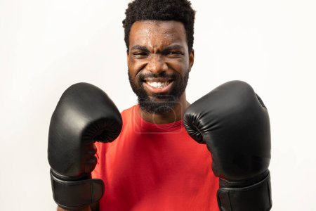 Téléchargez les photos : Portrait d'un homme afro-américain joyeux portant des gants de boxe, respirant la confiance et la vitalité, isolé sur un fond blanc. Représente un mode de vie sain et l'enthousiasme fitness. - en image libre de droit