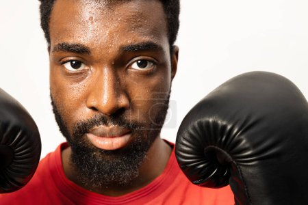 Téléchargez les photos : Gros plan d'un homme afro-américain déterminé avec des gants de boxe, montrant la concentration et la résilience. Parfait pour les thèmes de fitness et de motivation. - en image libre de droit