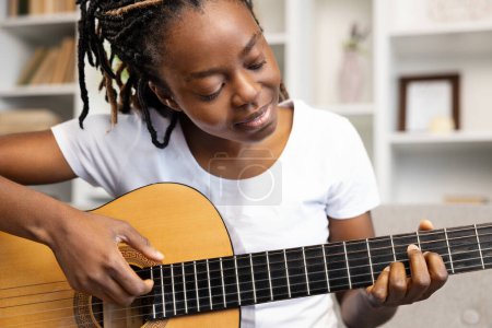Photo for Woman Practicing Guitar in a cozy home setting. In her leisure time, she indulges in her hobby, creating a relaxing and joyful atmosphere around her. - Royalty Free Image