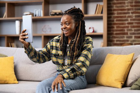 Foto de Mujer afroamericana participando en una animada videollamada en casa, mostrando una sensación de conexión y alegría mientras usa su tableta. - Imagen libre de derechos