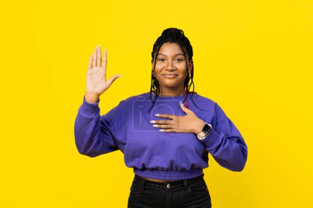 Foto de Afo mujer prometiendo, poniendo su mano sobre el corazón sobre un fondo amarillo vibrante, evocando confianza y sinceridad. - Imagen libre de derechos