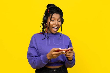 Foto de Mujer sorprendida e inmersa en la música, usando su smartphone con auriculares sobre un fondo amarillo brillante. - Imagen libre de derechos