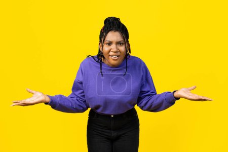 Foto de Mujer confusa haciendo gestos en suéter púrpura sobre un vibrante fondo amarillo. - Imagen libre de derechos