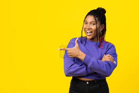 Téléchargez les photos : Femme pointant avec confiance quelque chose en pull violet vibrant sur un fond jaune. - en image libre de droit