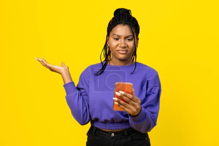 Woman puzzled by smartphon against a bright yellow background.